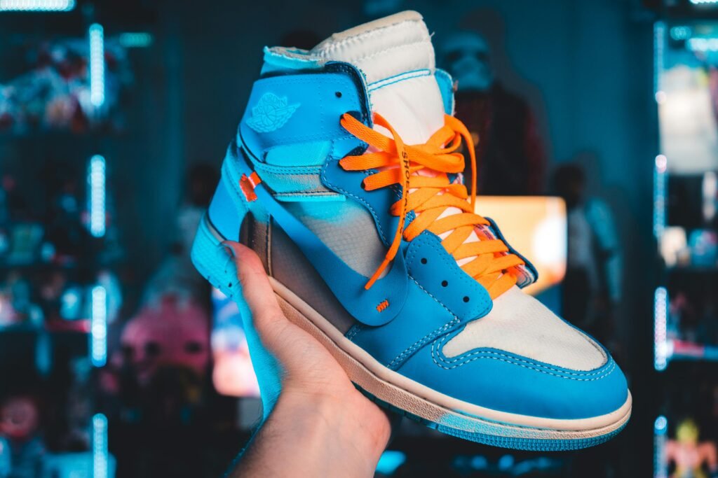 Close-up of a vibrant blue and orange Air Jordan 1 sneaker held in an illuminated setting.