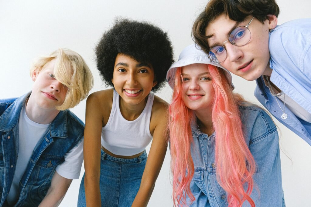Low angle of group of cheerful multiethnic teenager friends standing together against white background and looking at camera