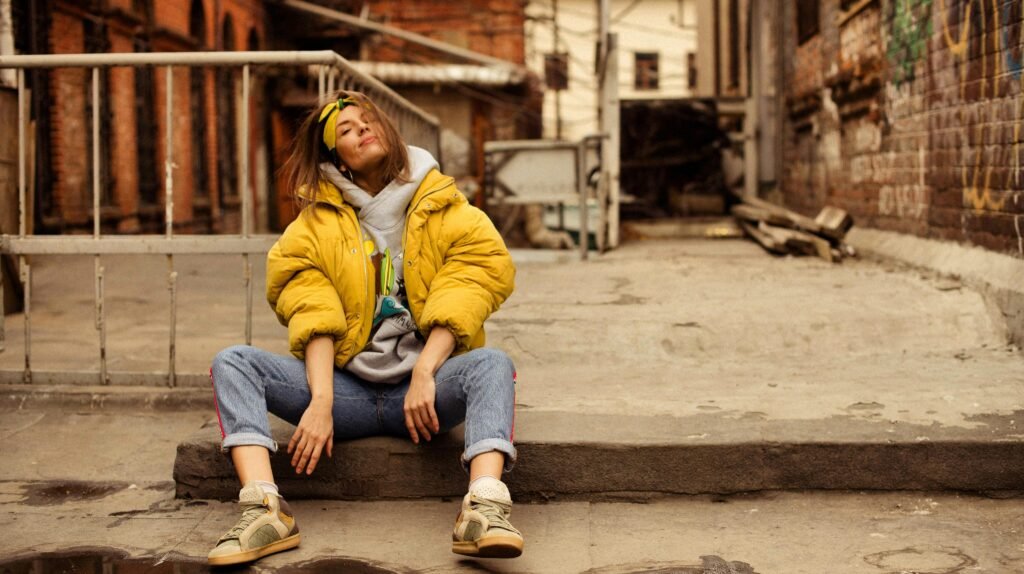 Woman in a yellow jacket sitting casually on a city sidewalk in Vladivostok.